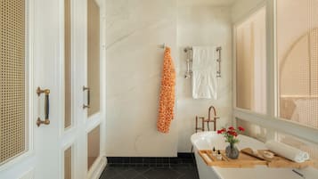 A bathroom with a bathtub, a sink, and a shower area. There are towels hanging on a rack, and a vase with flowers on the sink counter.