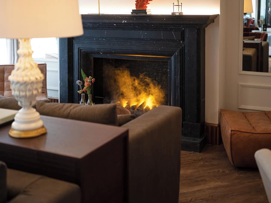 Una sala de estar con chimenea, un sofá, una mesa con lámpara y un jarrón decorativo.