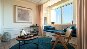 Una sala de estar moderna con un ventanal grande, un sofá azul, una silla de madera, una mesa de centro redonda y un mapa enmarcado en la pared.