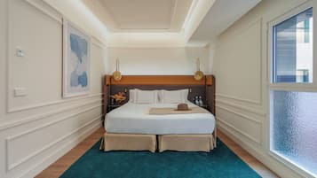 A hotel room with a large bed, a teal rug, a wooden headboard, and a window with frosted glass.
