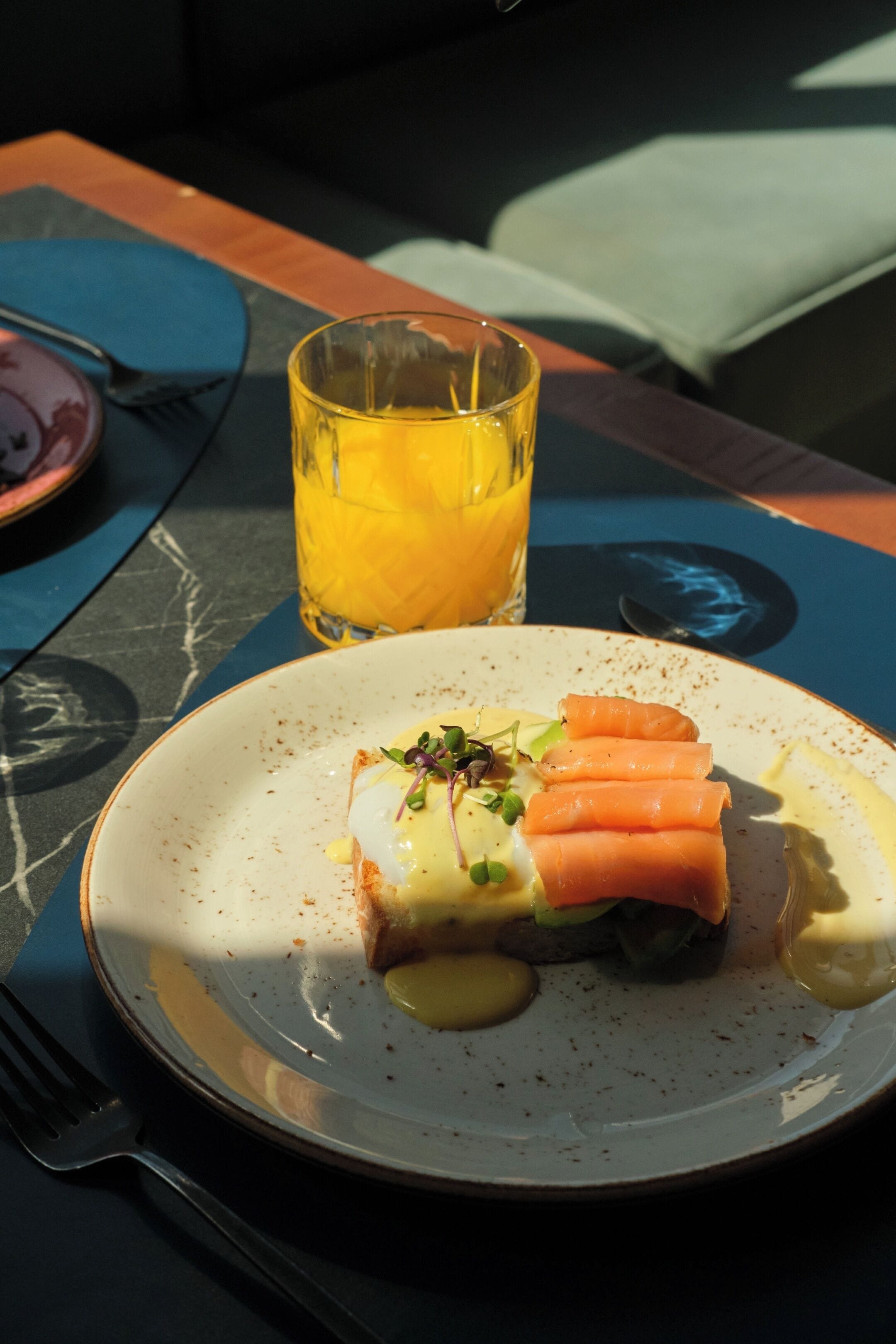 Un plato con comida, un vaso de jugo de naranja y un tenedor sobre una mesa.