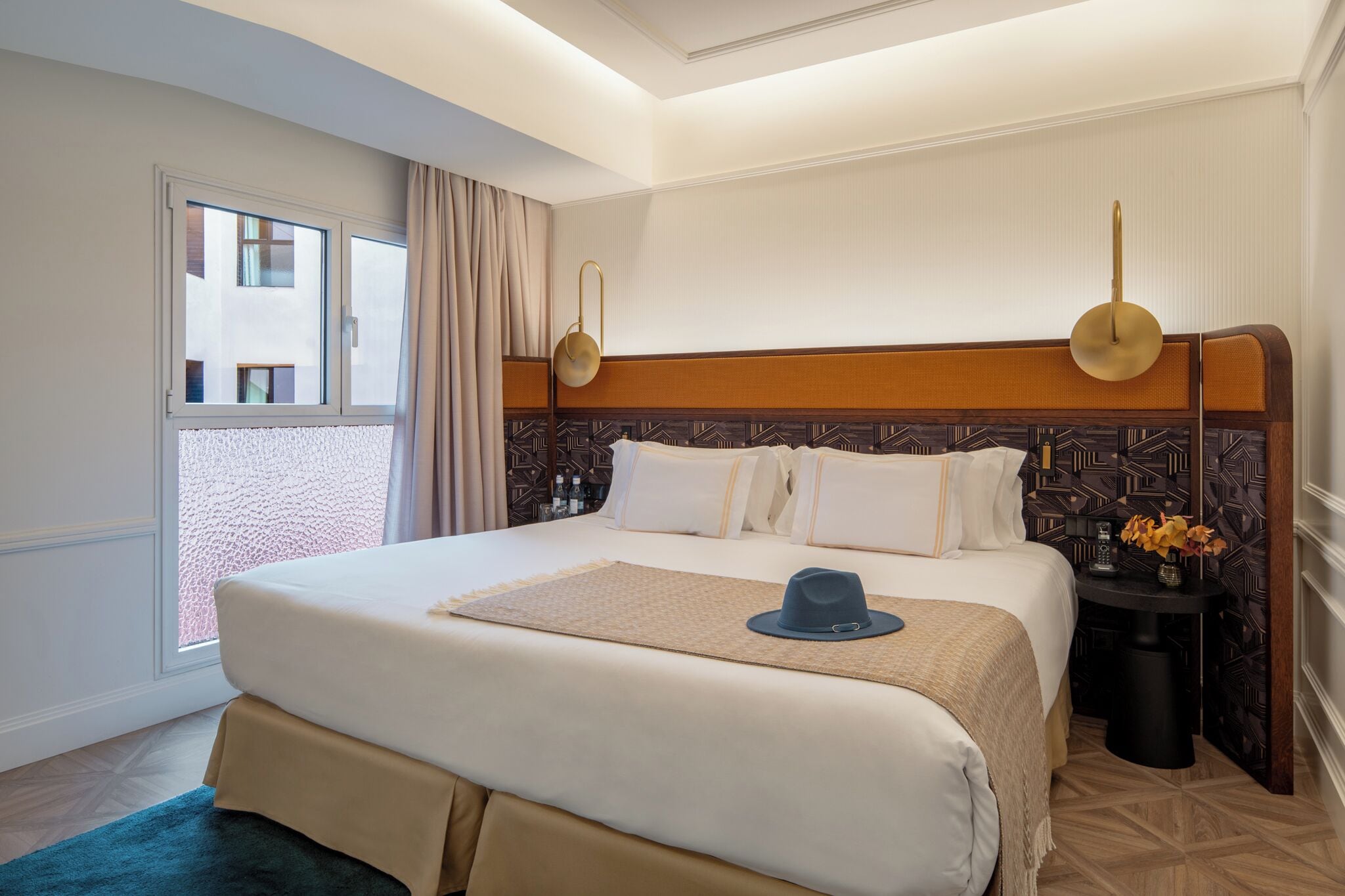 Ein Hotelzimmer mit einem großen Bett, einem Nachttisch mit einer Vase und Blick ins Freie.