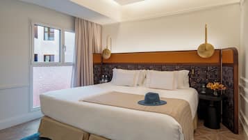Habitación de hotel con una cama grande, una mesita de noche con un florero y vistas al exterior.