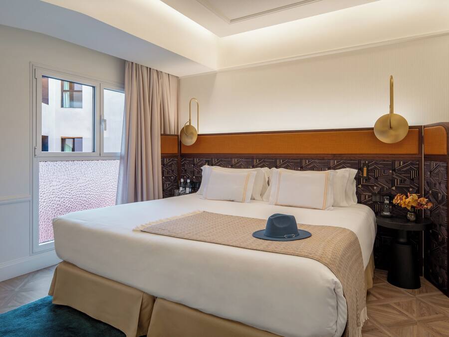 Habitación de hotel con una cama grande, una mesita de noche con un florero y vistas al exterior.