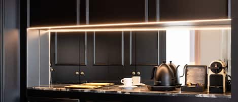 A modern kitchen with black cabinetry, a marble countertop, a coffee maker, and a kettle.