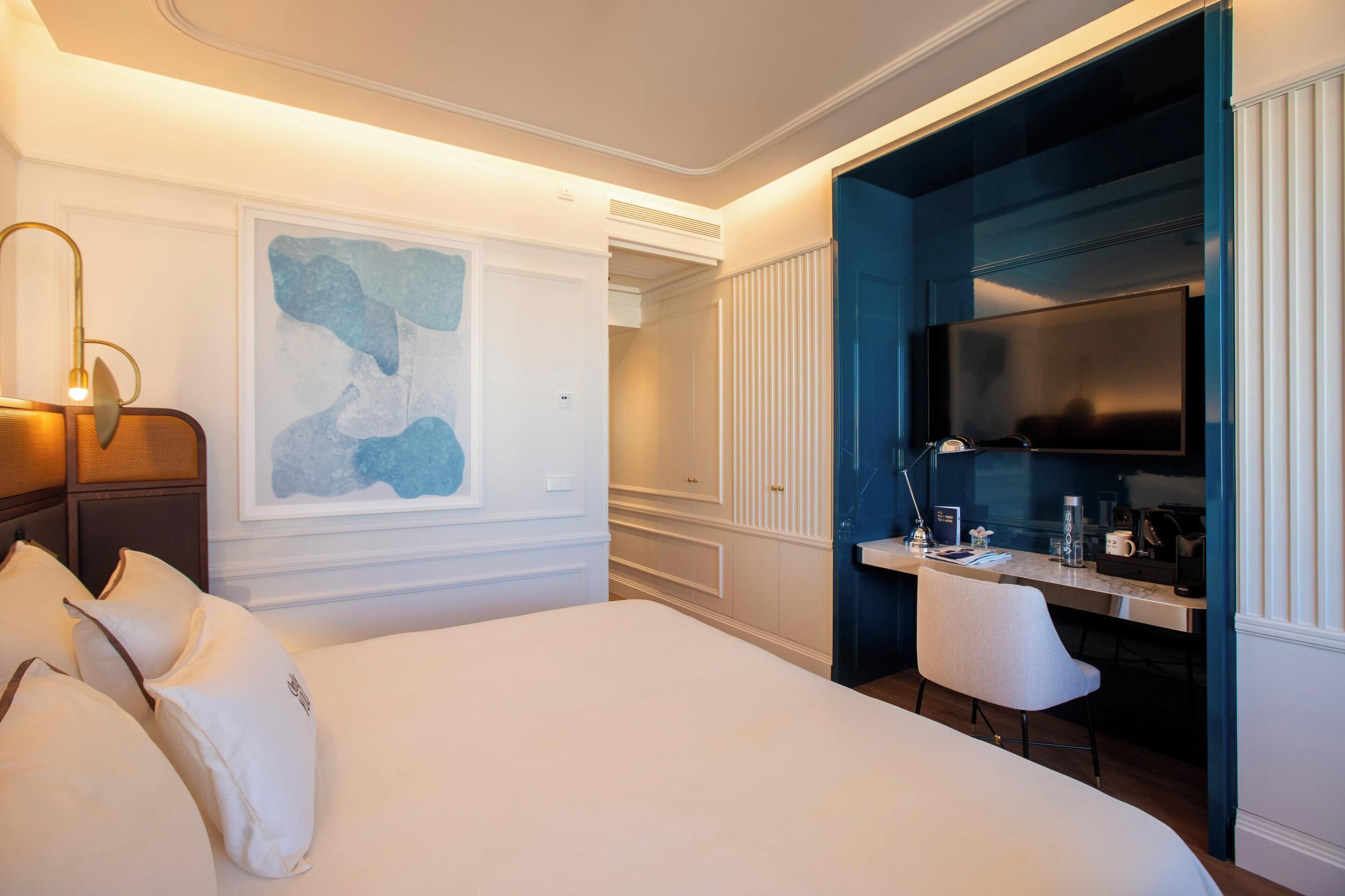 Habitación de hotel con una cama grande, un escritorio con televisor de pantalla plana y una obra de arte moderno en la pared.