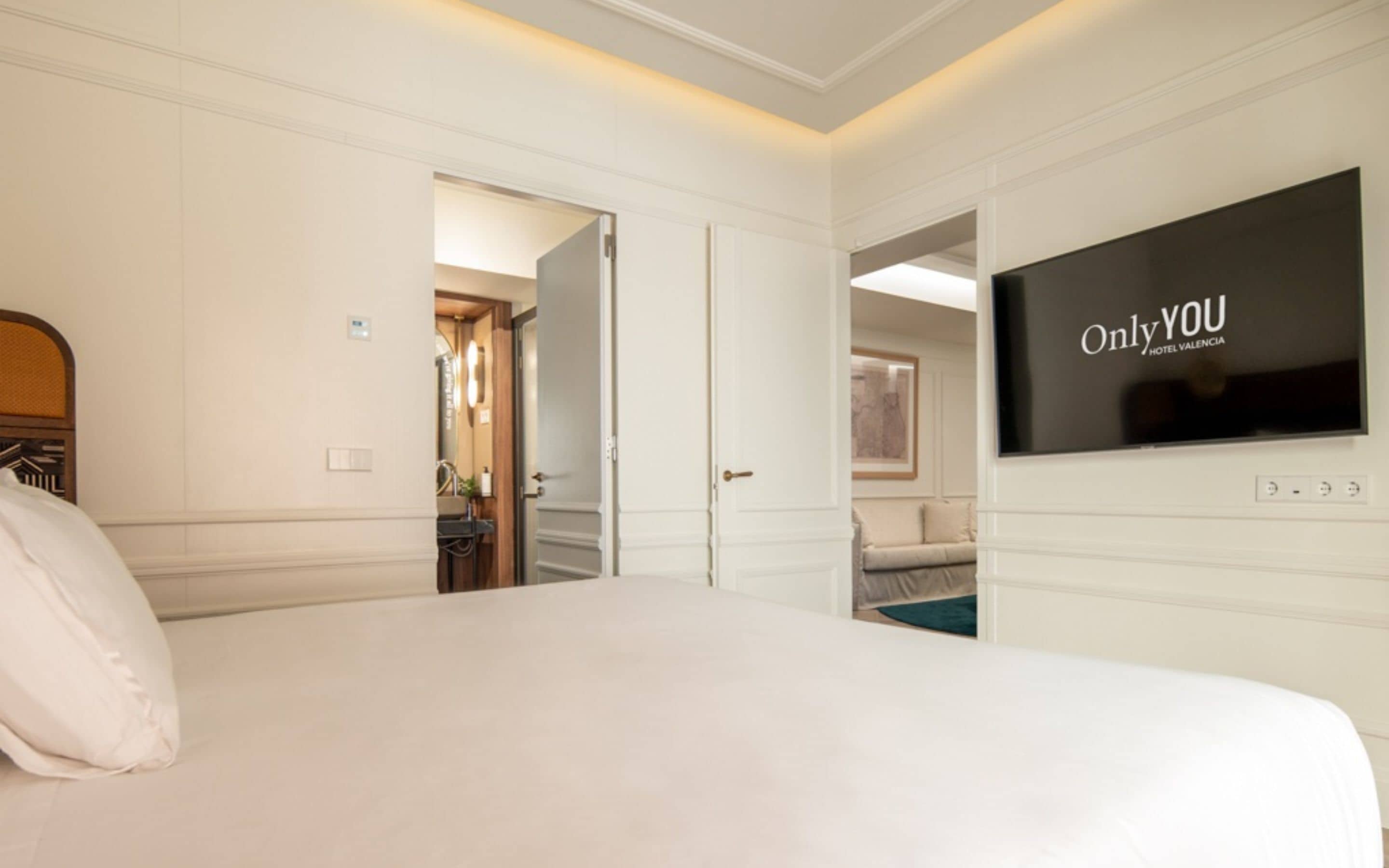 A hotel room with a large bed, a TV on the wall, and a door leading to a bathroom.