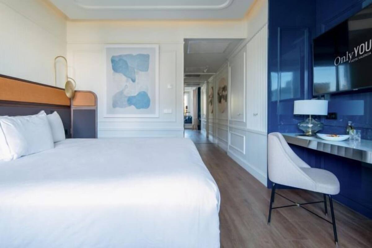 A hotel room with a large bed, a desk with a chair, and a wall-mounted TV.