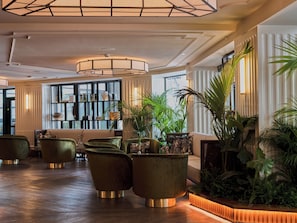 Un vestíbulo con diseño moderno, que cuenta con una zona de estar con sillones tapizados en verde, una gran planta en maceta y una pared decorativa con estanterías.
