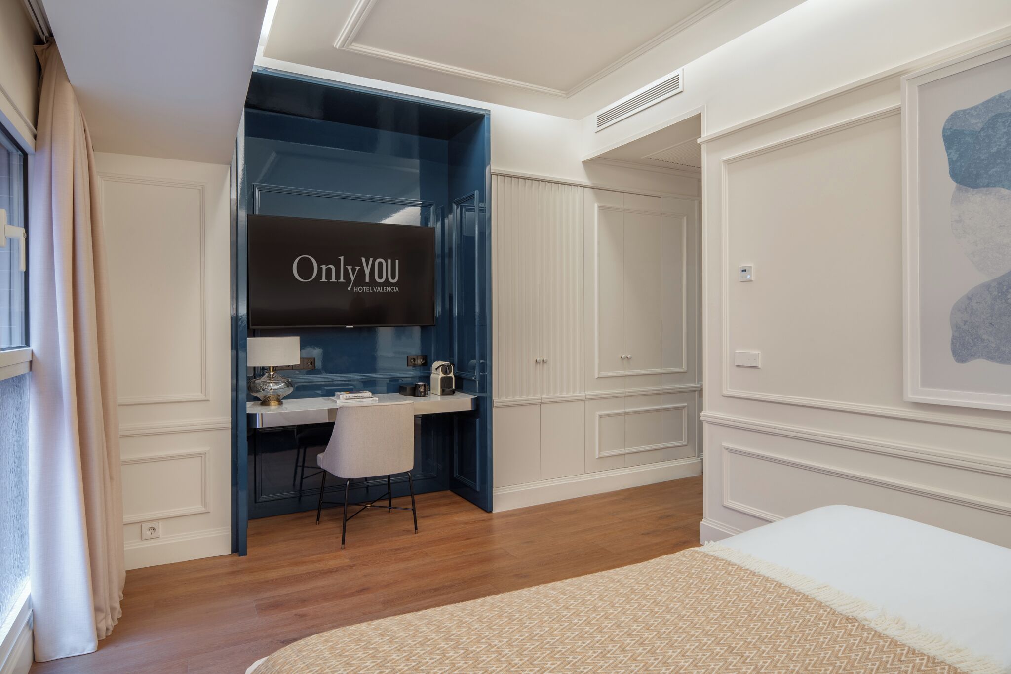 A hotel room with a bed, a desk with a chair, a television, and a wardrobe.