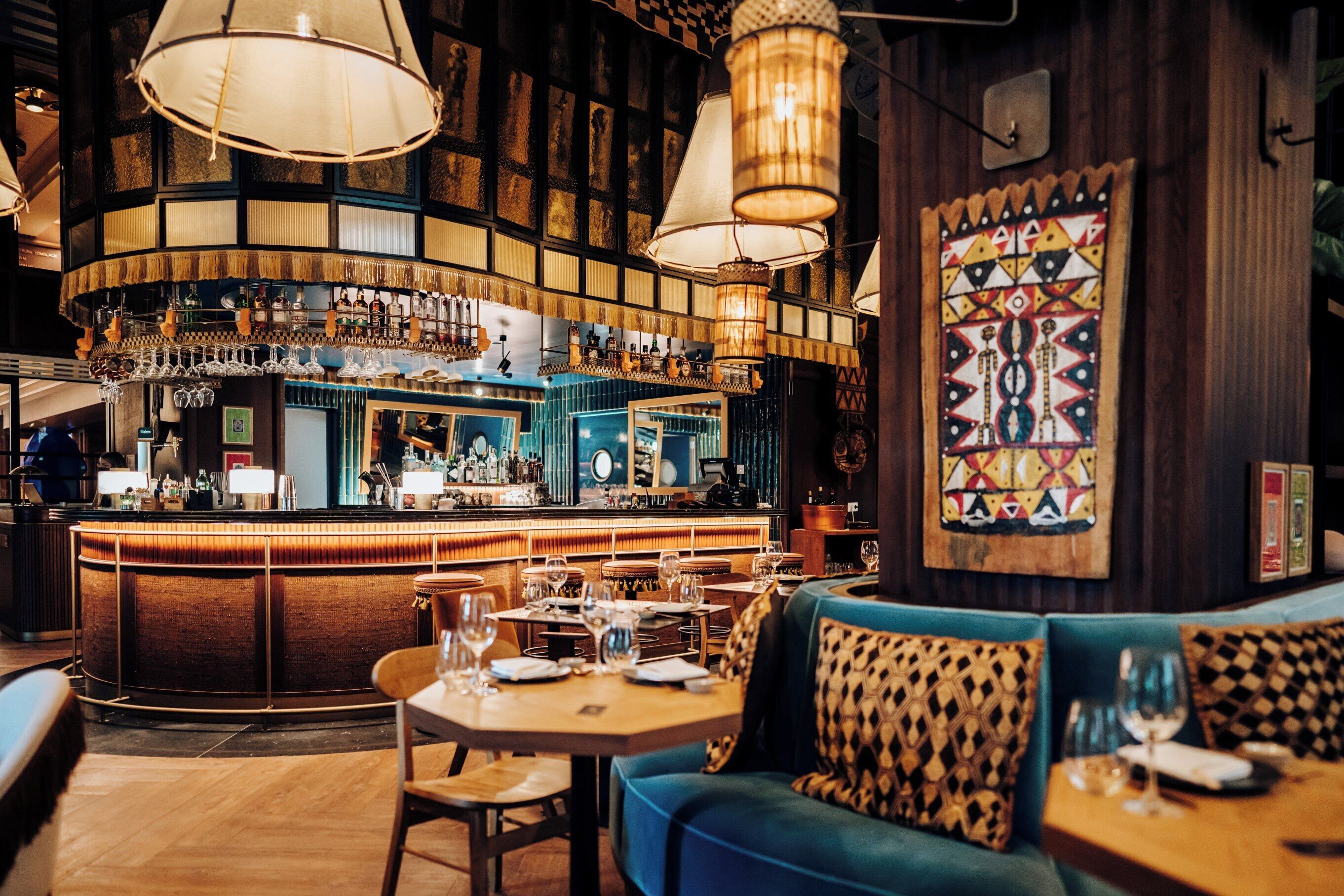 Zona de bar con barra, vasos colgantes y área de asientos con pared decorada.