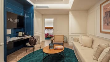 Habitación de hotel moderna con televisor, escritorio, silla, sofá y una ventana grande.