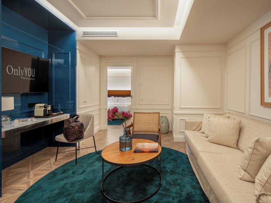 Habitación de hotel moderna con televisor, escritorio, silla, sofá y una ventana grande.