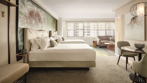 Een moderne hotelkamer met een groot bed, een bank, een eettafel en een groot raam met uitzicht op de stad.