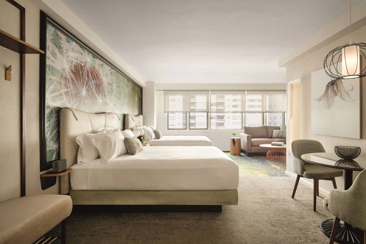 Una habitación de hotel moderna con una cama grande, un sofá, una mesa de comedor y un ventanal con vistas a la ciudad.