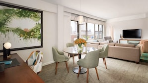 Een moderne woonkamer met een ronde glazen tafel, twee groene stoelen, een beige bank en een tv op een meubel.