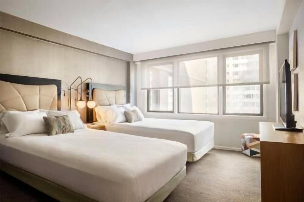 Habitación de hotel con dos camas, un ventanal grande y un escritorio.
