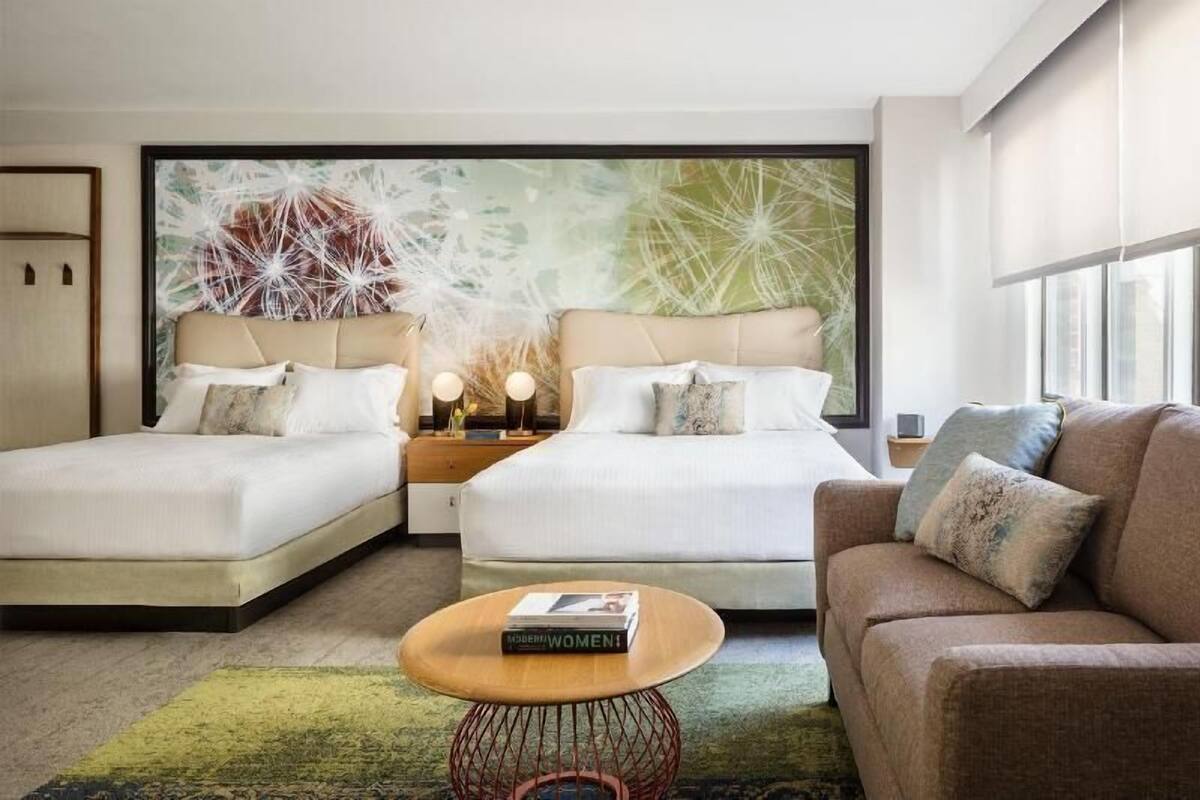 Una habitación de hotel moderna con dos camas, un sofá, una mesa de centro y una gran obra de arte abstracta en la pared.