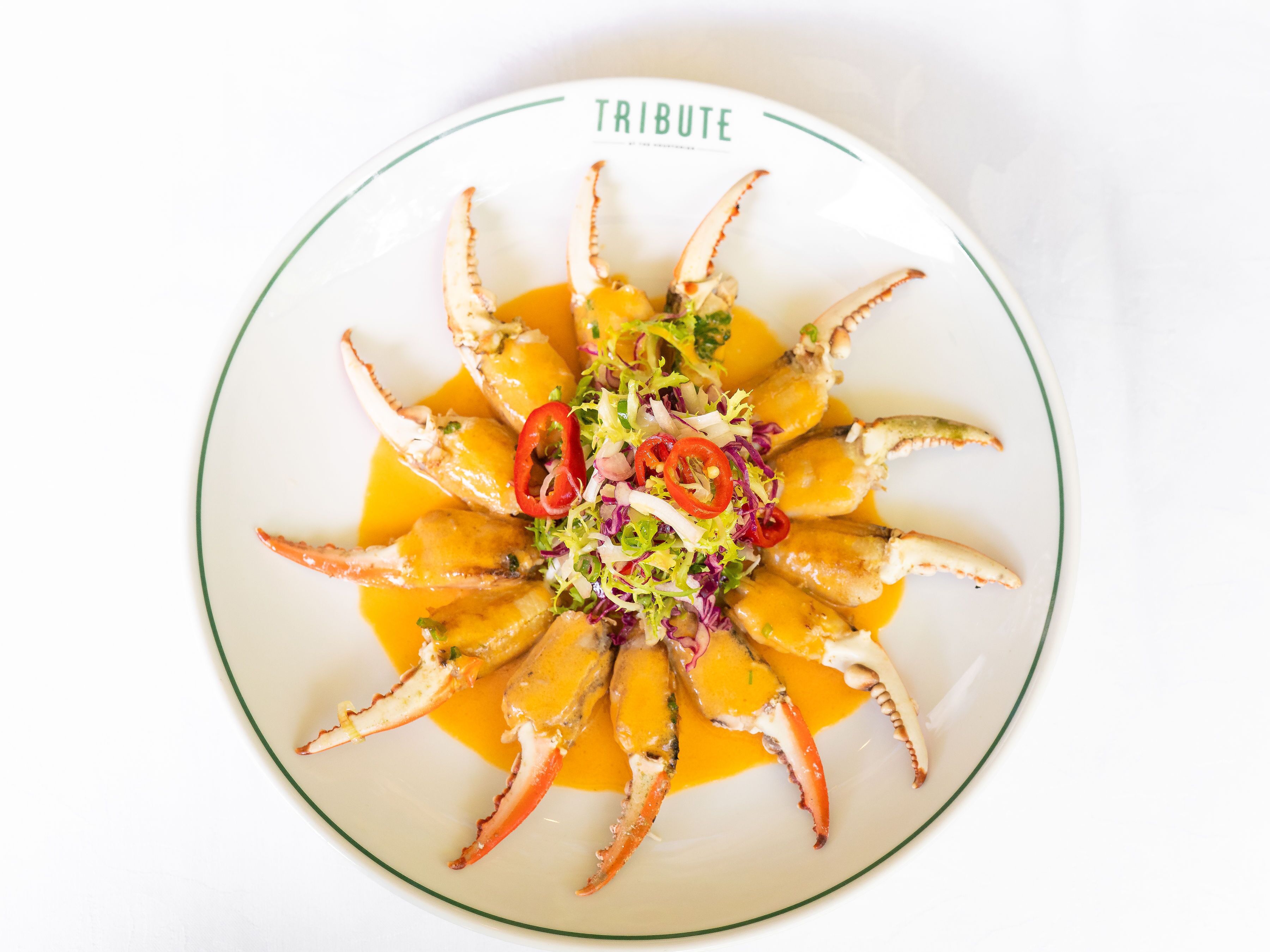 Un plato de patas de cangrejo dispuestas en círculo, con guarnición de verduras y salsa.