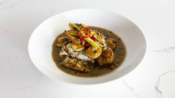 A white plate with a dish containing meat, vegetables, and a dark sauce on a marble surface.