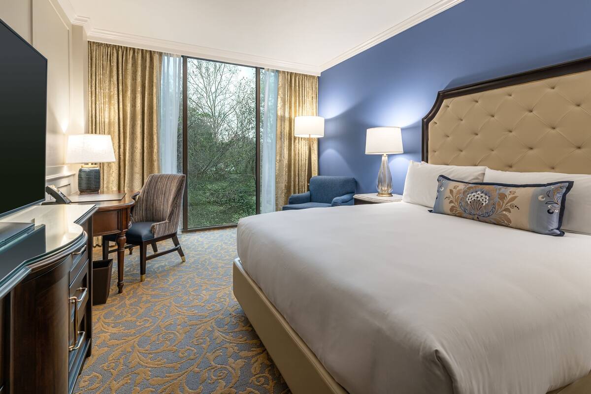Une chambre d’hôtel avec un grand lit, un bureau avec une chaise, une télévision et une fenêtre avec des rideaux.