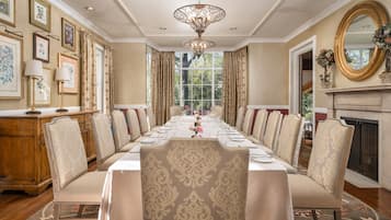 Un comedor formal con una larga mesa dispuesta para una comida, flanqueada por sillas ornamentadas, un candelabro y obras de arte enmarcadas en las paredes.
