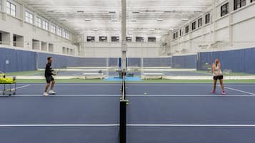 An indoor tennis court with a high ceiling, multiple tennis courts, and seating areas.