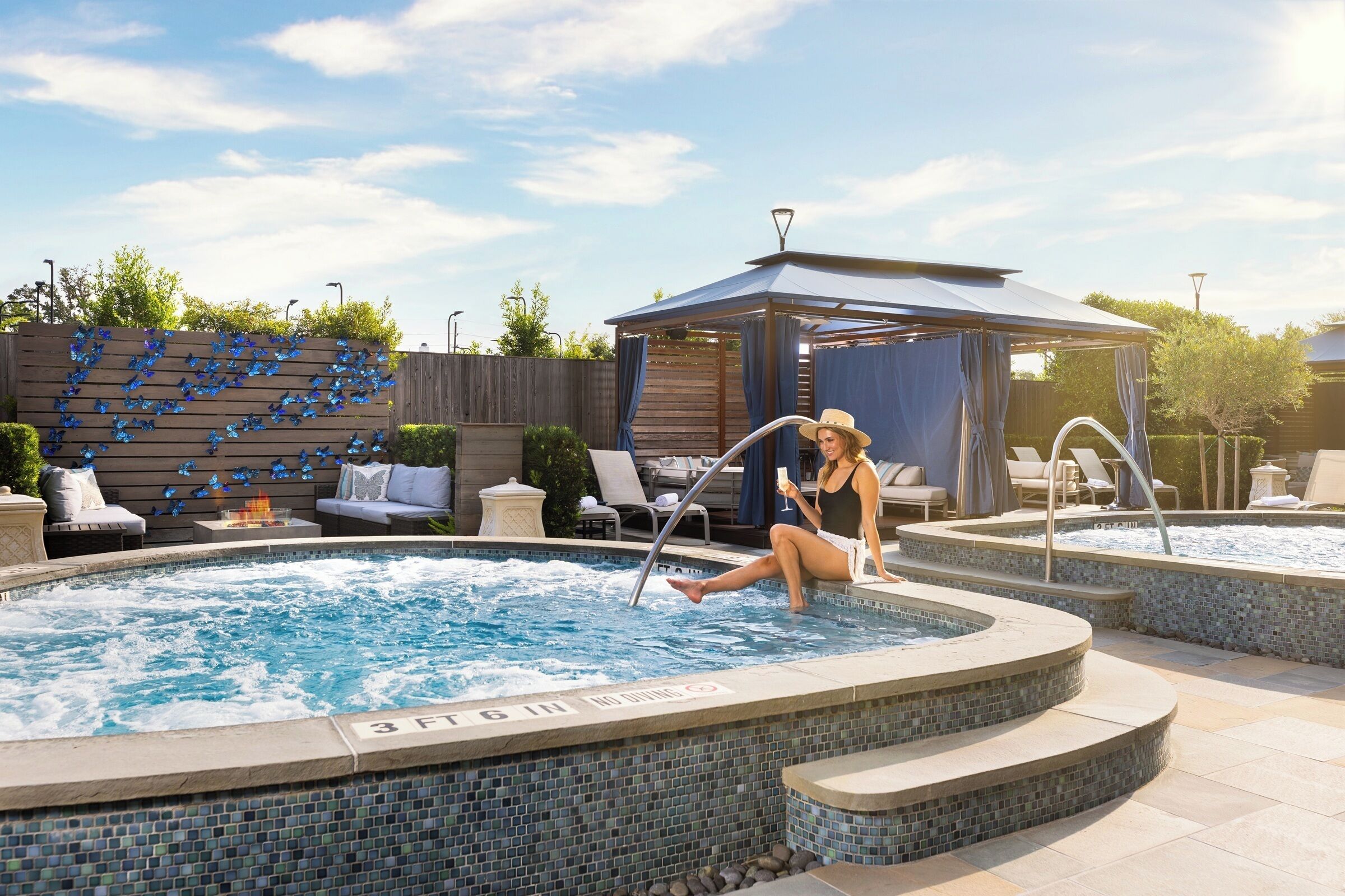 A swimming pool with a tiled edge, lounge chairs, a gazebo, and a wooden fence with butterfly decorations.
