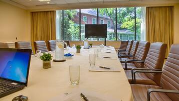 A conference room with a long table, chairs, a laptop, and a TV.