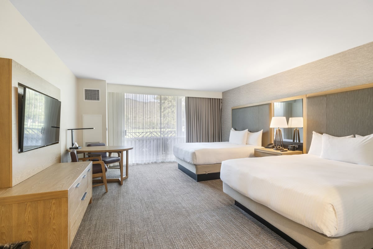 Habitación de hotel con dos camas, un escritorio, una silla, un televisor y una ventana con cortinas.