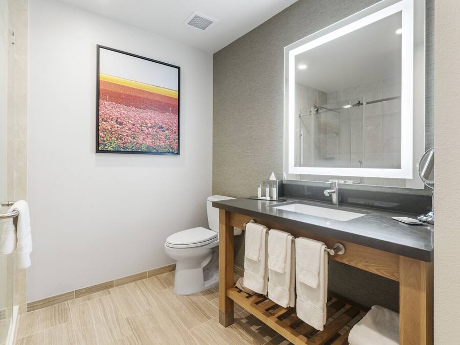 A modern bathroom with a toilet, sink, and shower. There is a framed picture on the wall and a towel rack with towels.