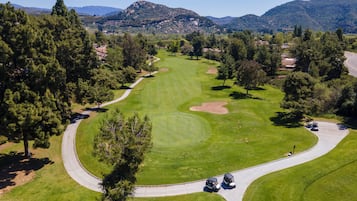 A golf course with a winding path, trees, and distant mountains.