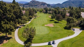 A golf course with a winding path, trees, and distant mountains.