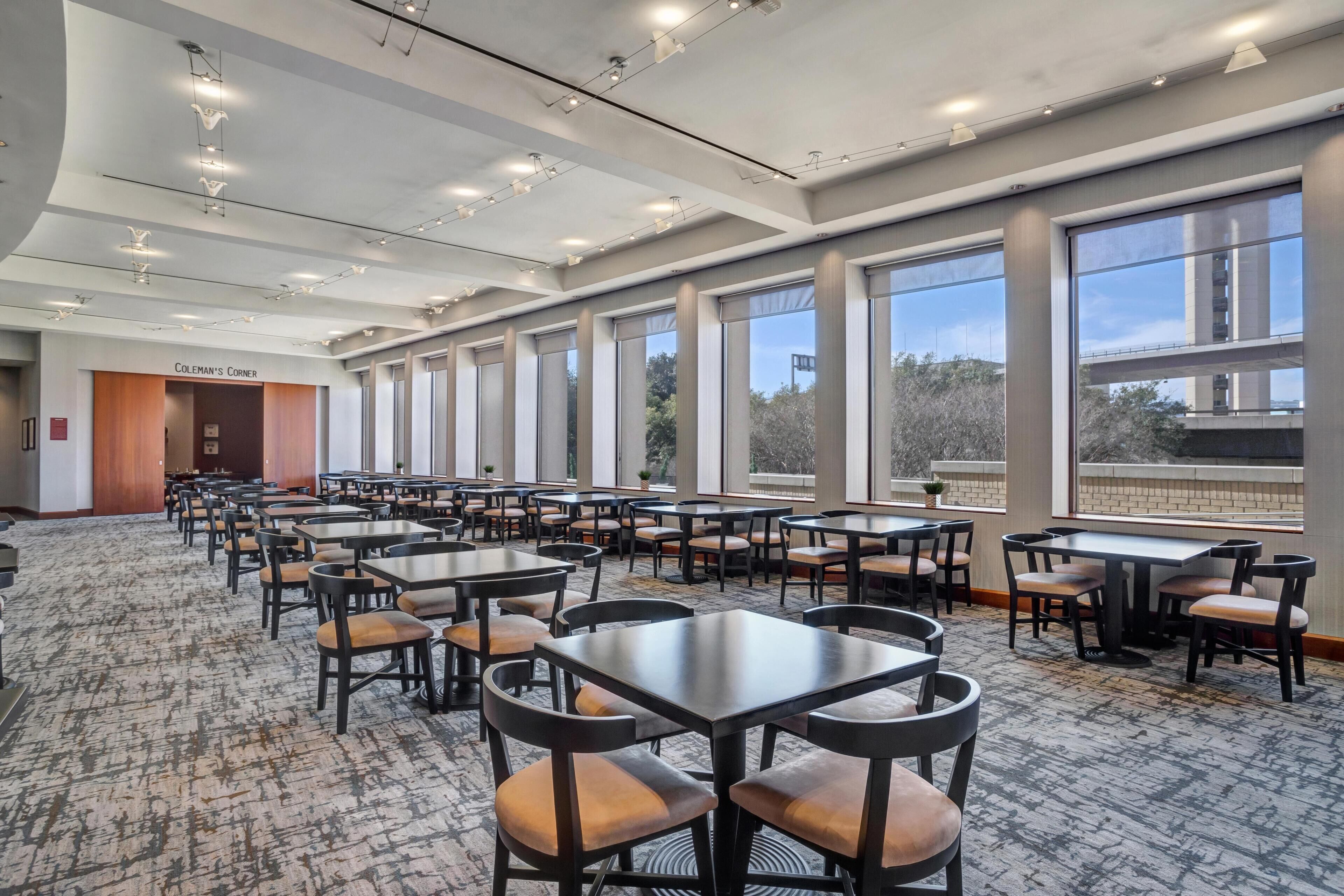 A spacious indoor area with multiple tables and chairs, large windows, and a visible entrance labeled 'COLEMAN'S CORNER'.