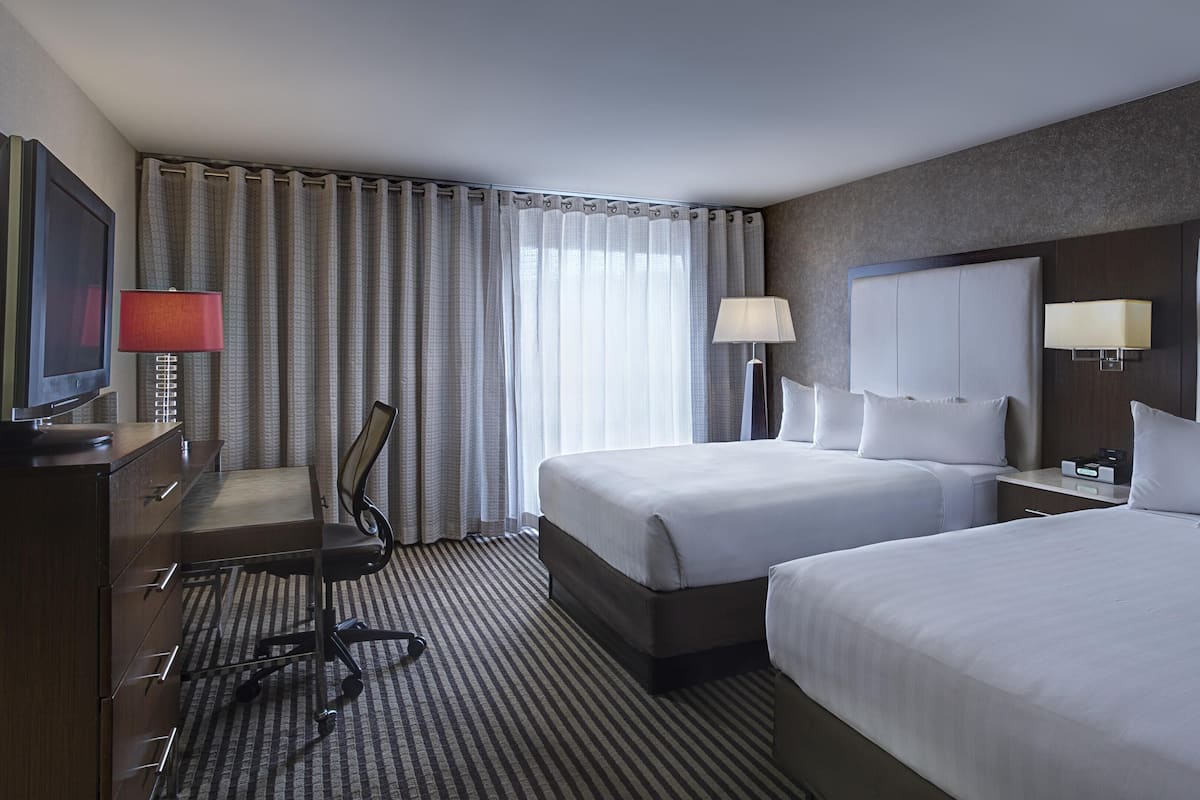 A hotel room with two beds, a desk with a chair, a television, and a lamp.