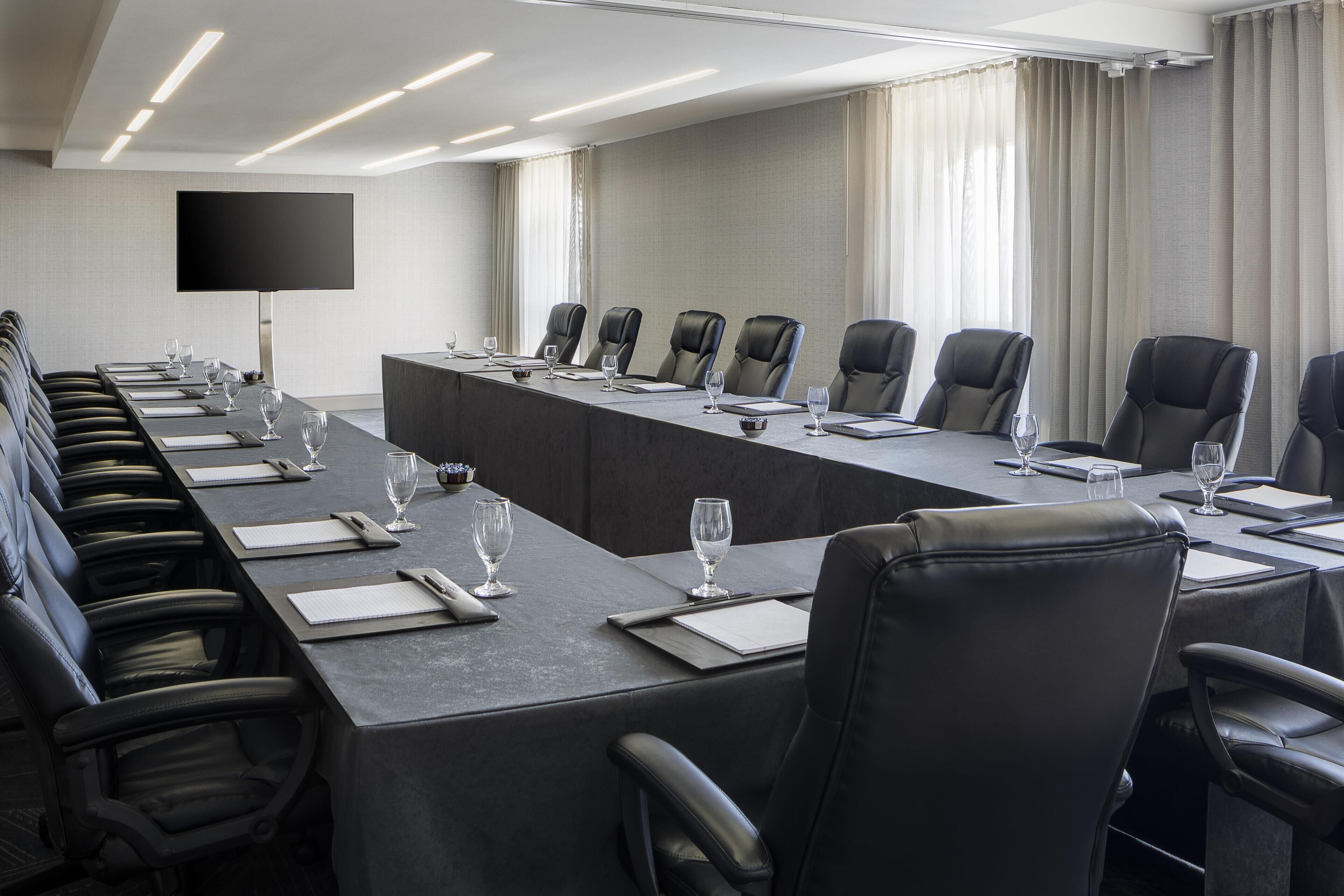 A conference room with a long table, black leather chairs, and a flat-screen TV on the wall.