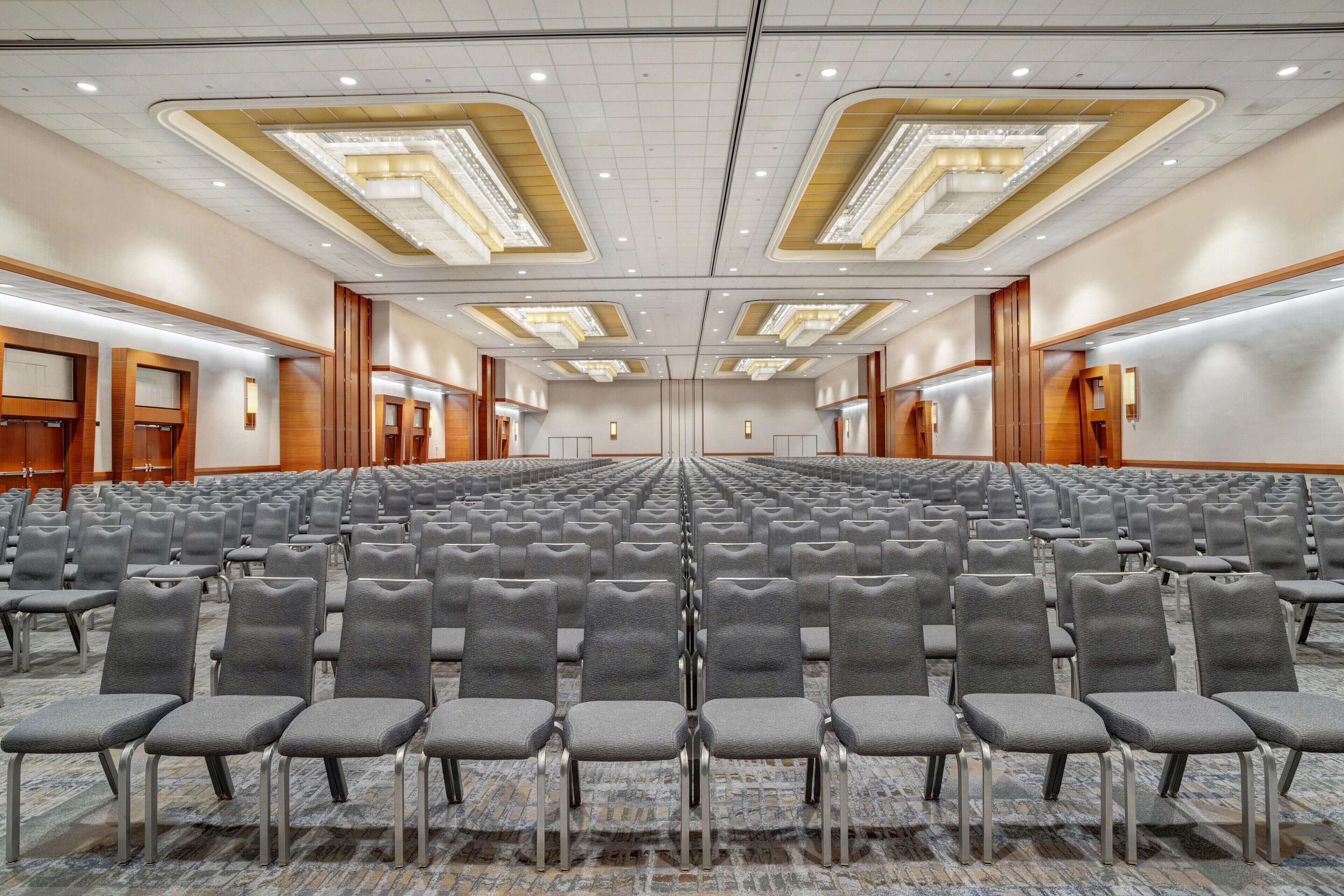 A conference room with rows of grey chairs, a patterned carpet, and a ceiling with recessed lighting.