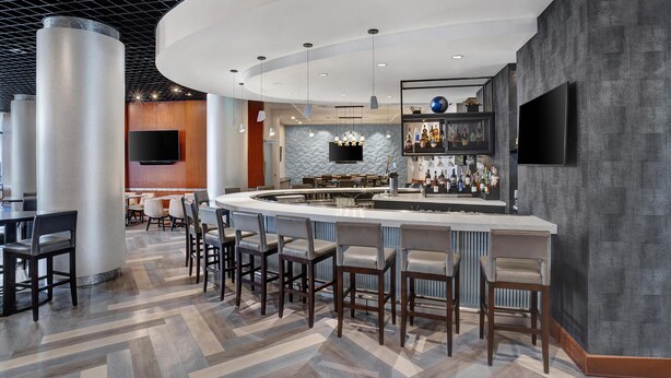 A modern bar area with a curved counter, bar stools, a flat-screen TV, and a wall-mounted liquor display. - Hyatt Regency DFW International Airport - Adjacent to Terminal C (Dallas)