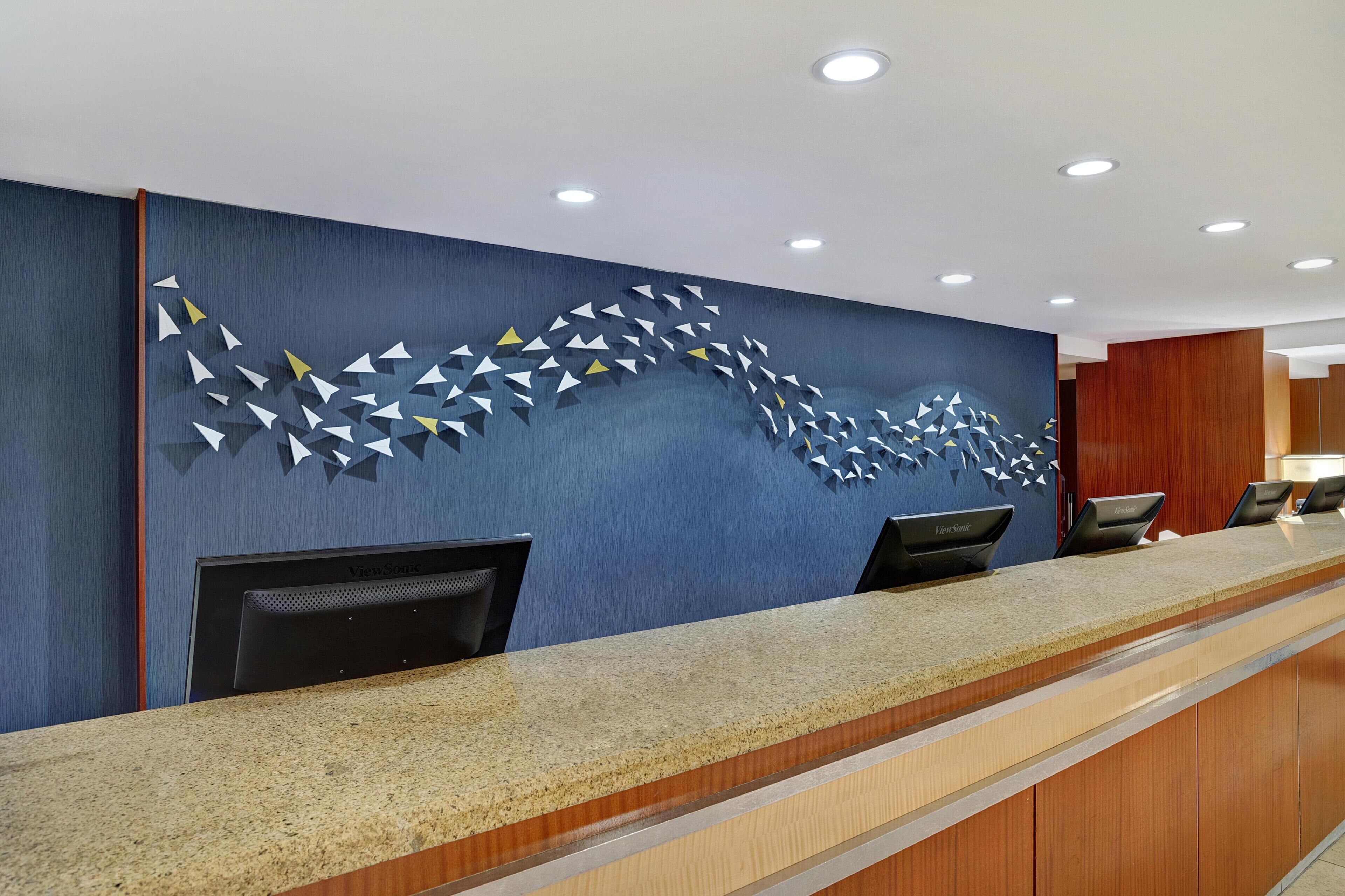 A reception desk with a blue wall and a geometric pattern, three black chairs, and a wooden counter.