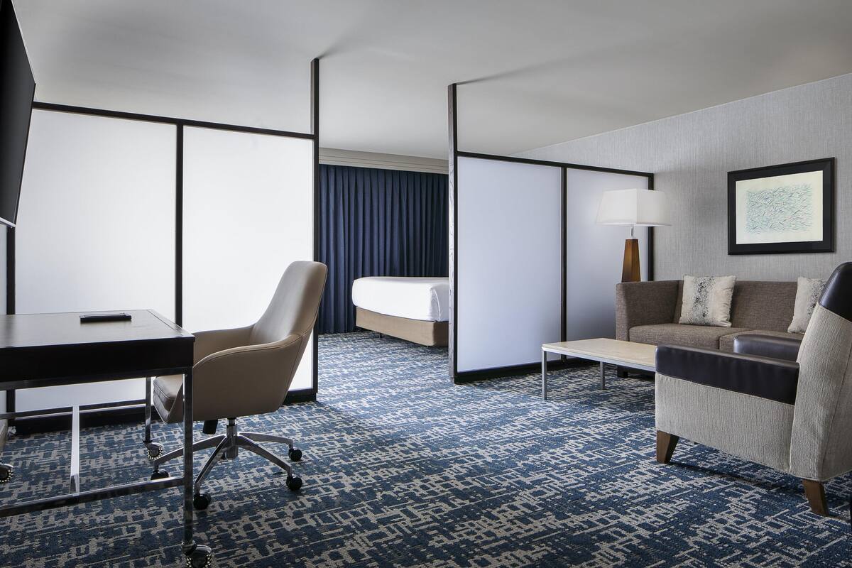 A hotel room with a bed, a desk, a chair, a sofa, a lamp, and a framed picture on the wall.