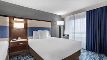 Habitación de hotel con una cama grande, una mesita de noche con lámpara, un escritorio con teléfono y una ventana con cortinas.