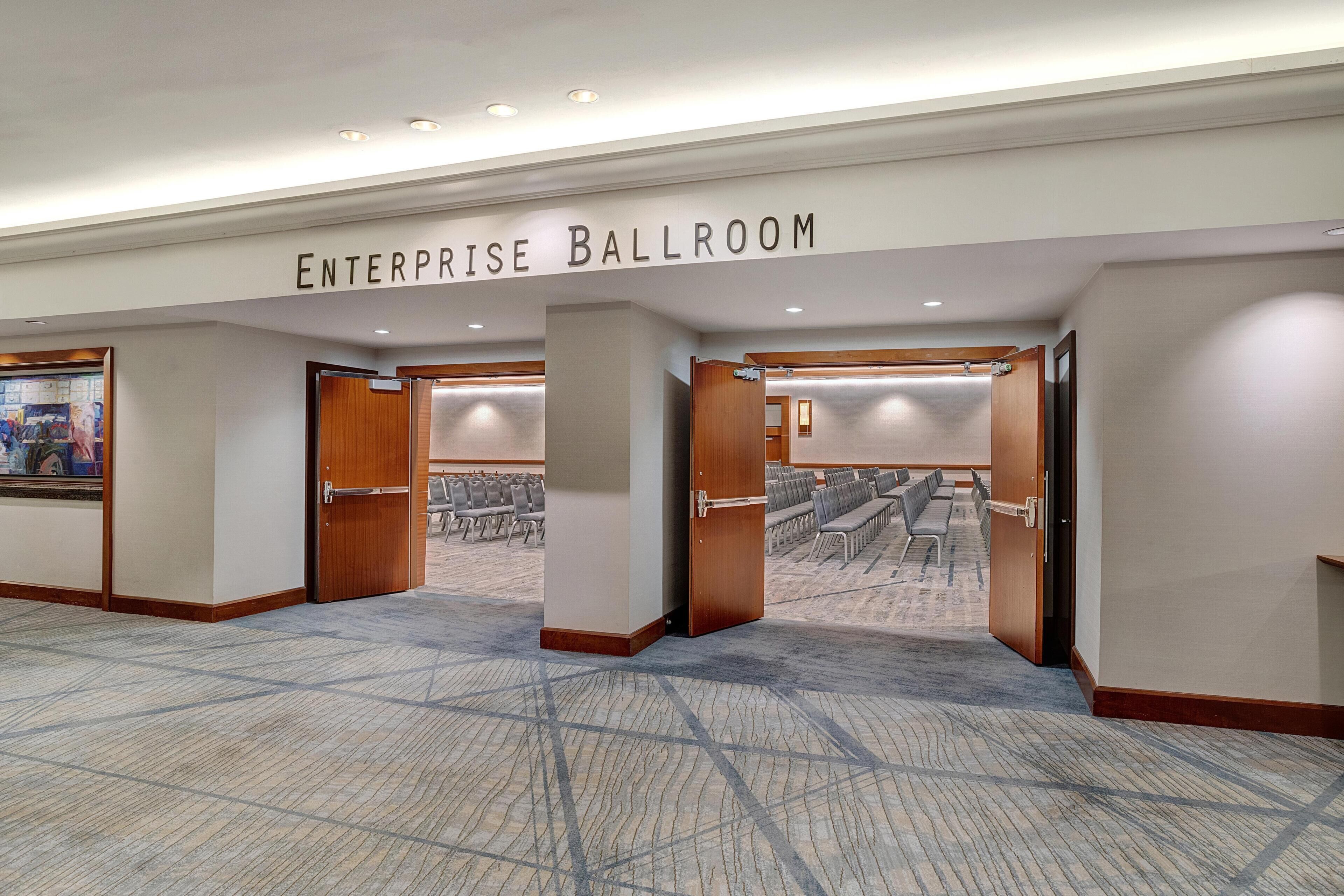 An enterprise ballroom with a carpeted floor, wooden doors, and a sign above.