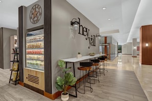 A modern café with a refrigerated display, bar stools, and a wall with 'hey y'all' signage.