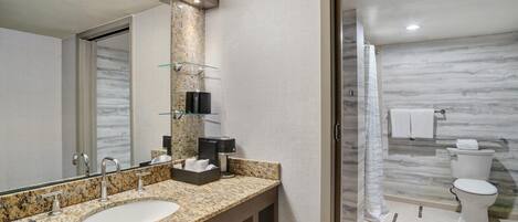 A modern bathroom with a granite countertop, a large mirror, a sink, a toilet, and a shower area.