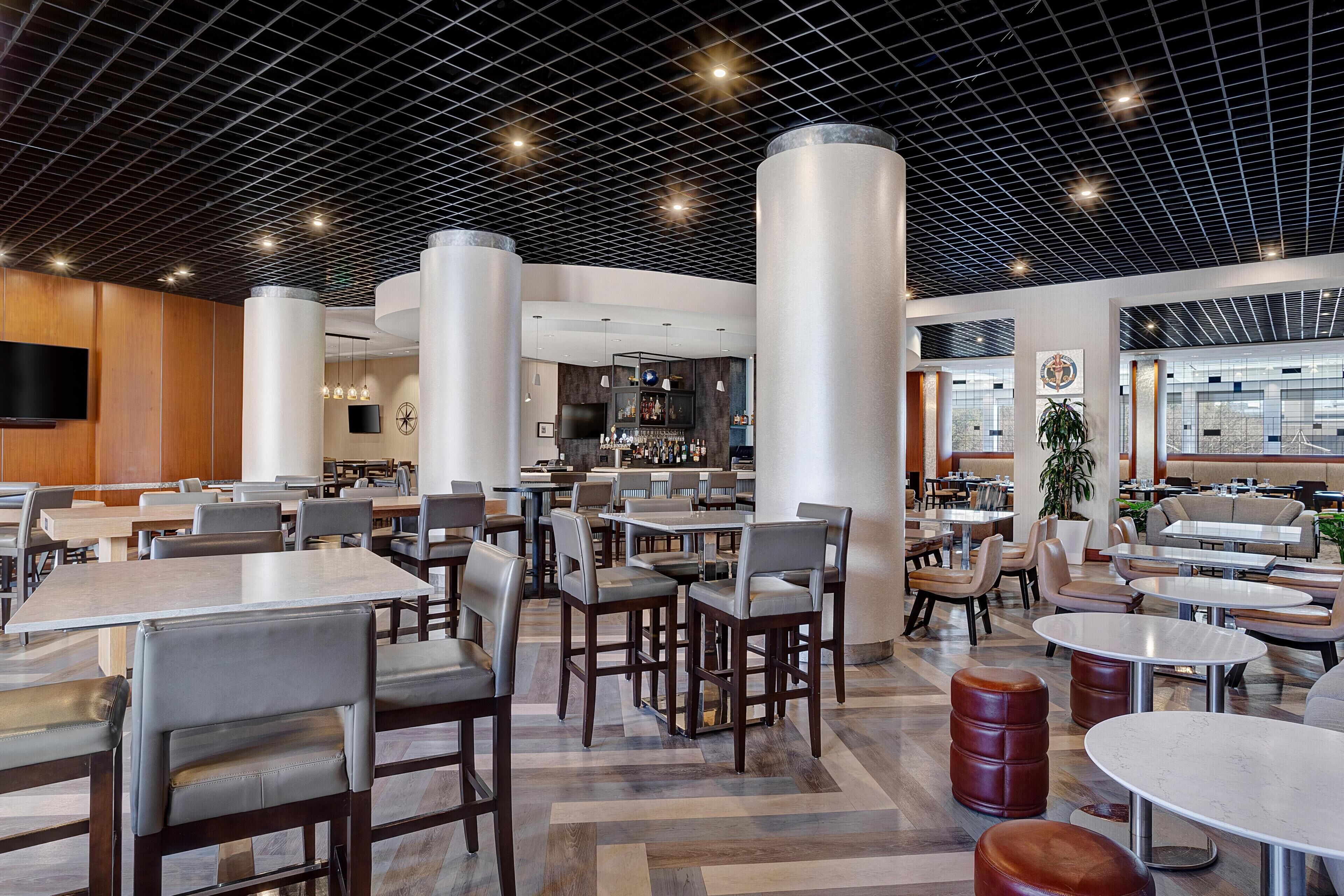 A spacious indoor area with multiple seating arrangements, including tables and chairs, and a bar area with shelves of bottles.
