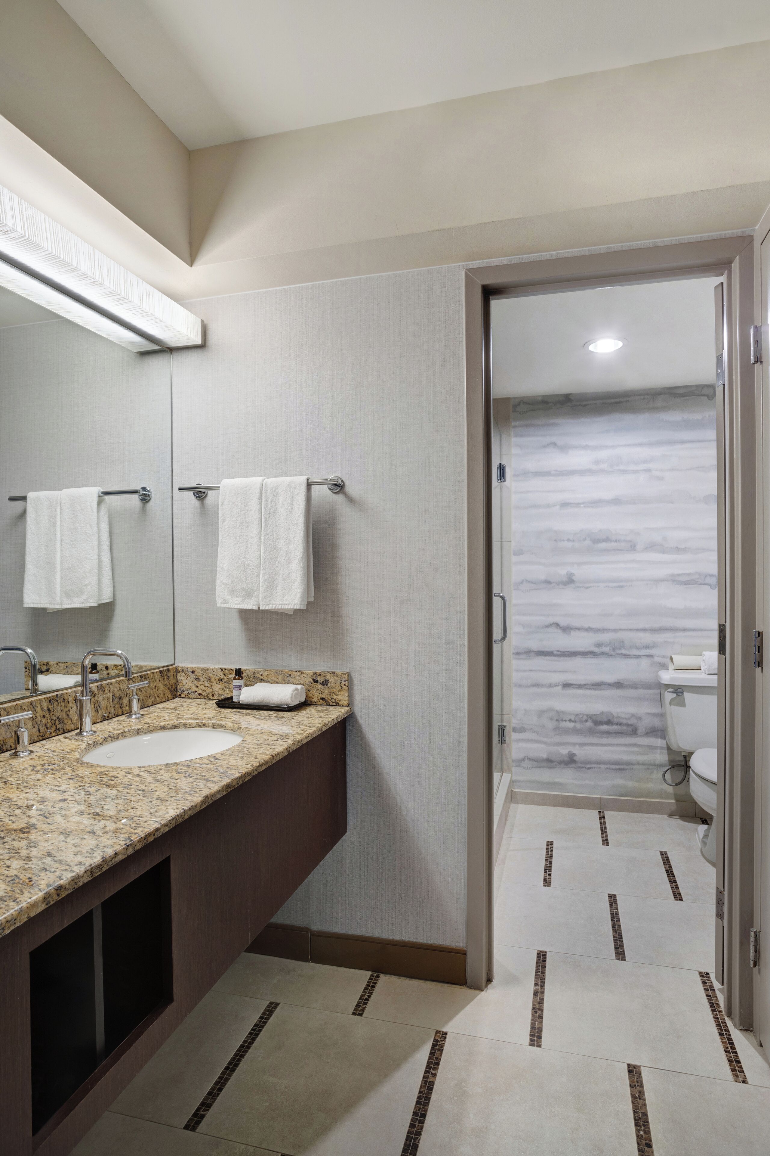 A modern bathroom with two sinks, a mirror, and a toilet visible through an open door.