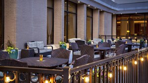 An outdoor seating area with wicker furniture and potted plants, a brick wall, and a view of the interior. - Hyatt Regency DFW International Airport - Adjacent to Terminal C (Dallas)