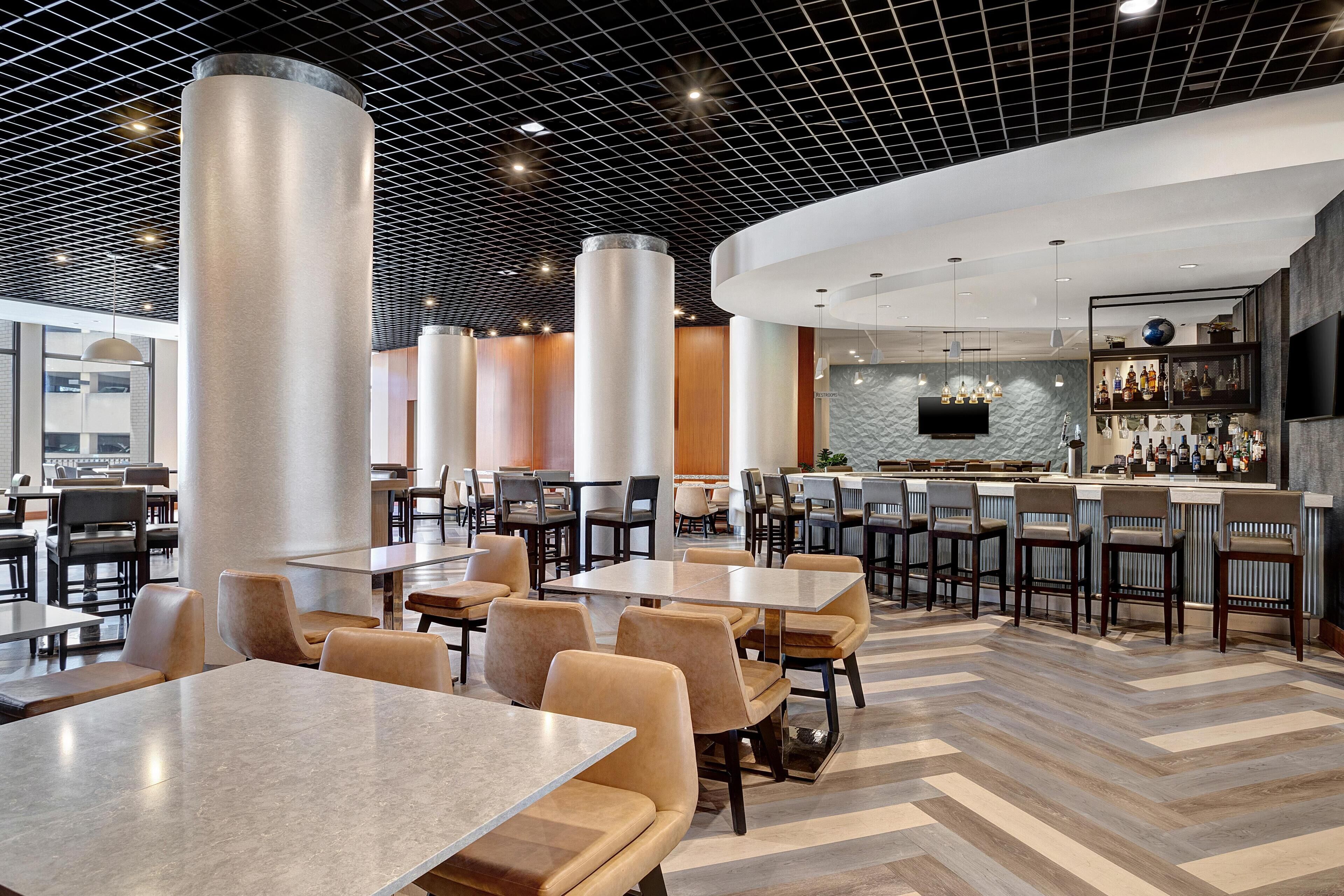A modern restaurant with high ceilings, a bar area, and multiple seating arrangements.