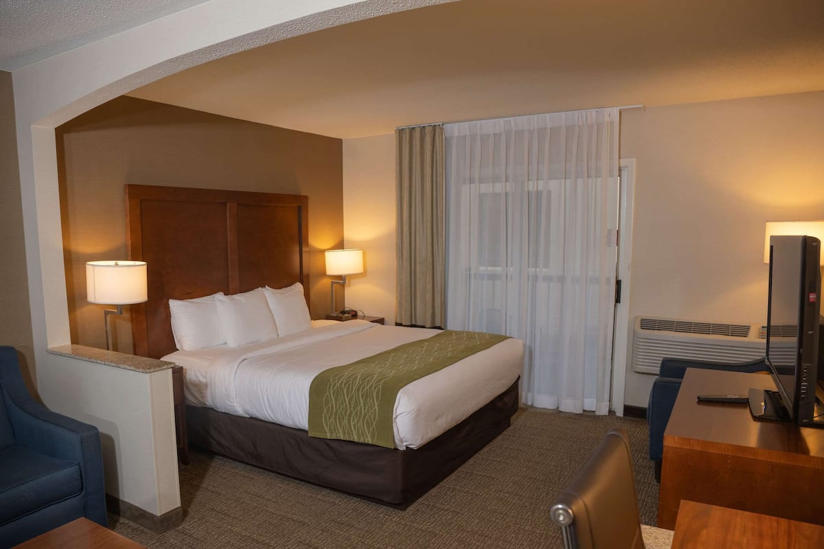 A hotel room with a bed, two bedside lamps, a desk with a computer, and a chair.
