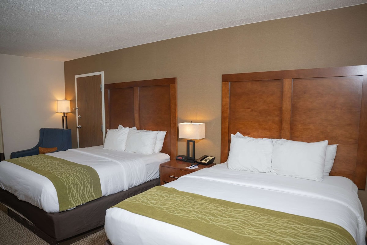 A hotel room with two beds, a desk, a chair, and a lamp.